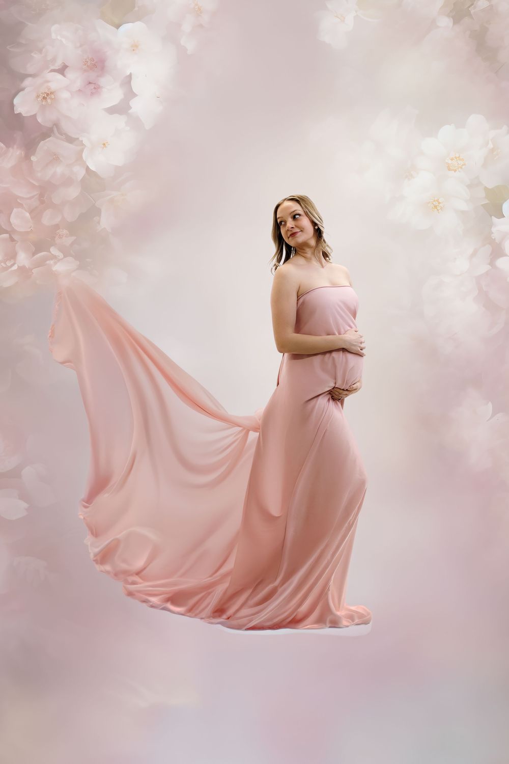A dreamy maternity photo series showing a woman in a flowing pink gown against a soft floral backdrop.