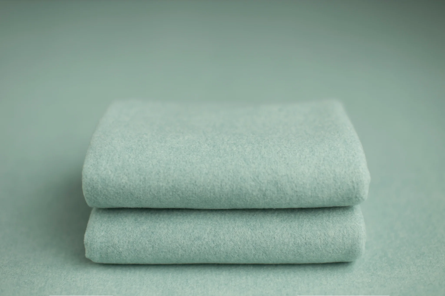 Two folded mint green soft blankets stacked on matching background.