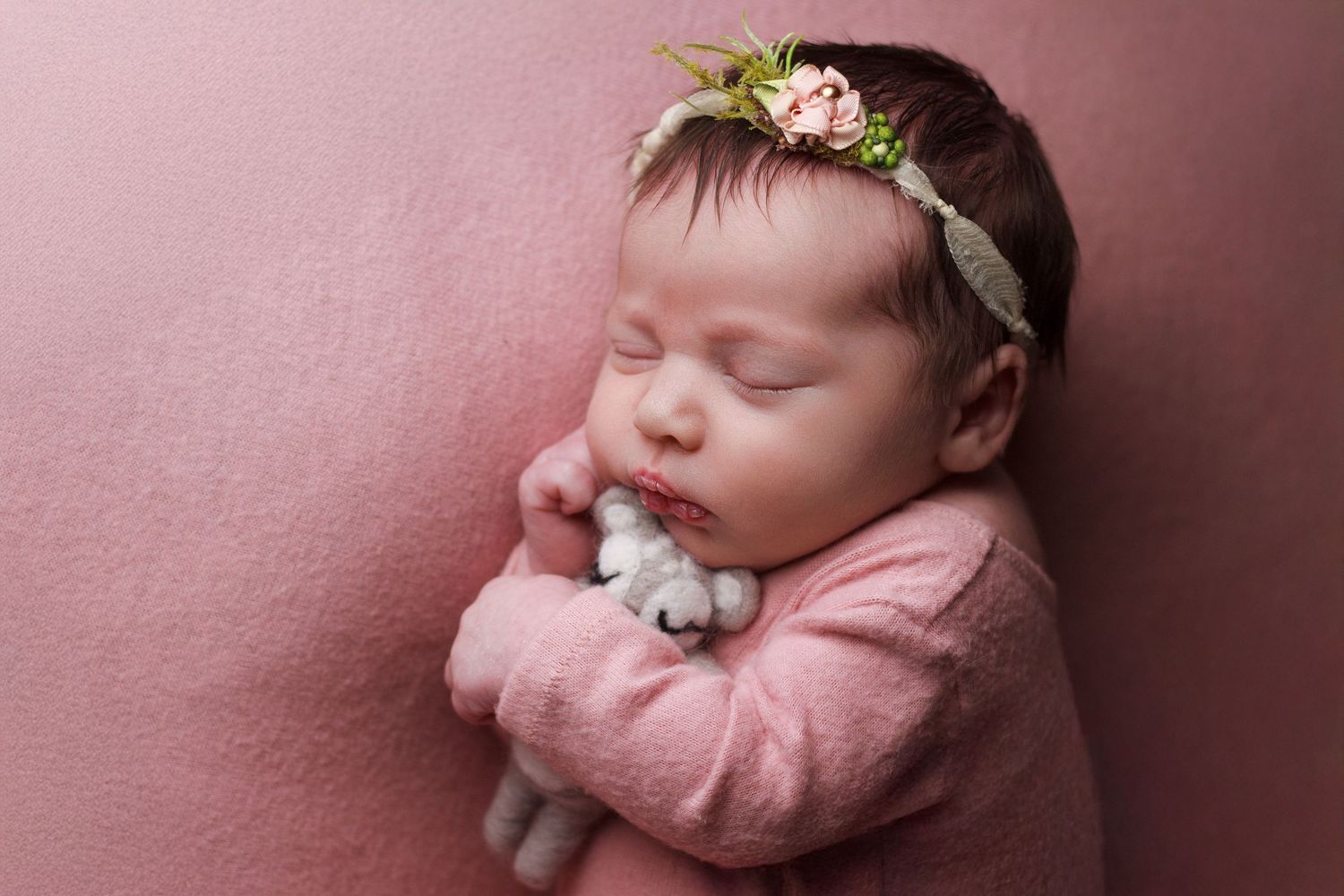 Newborn baby girl wearing a blush pink sleeper laying on a blush pink backdrop.