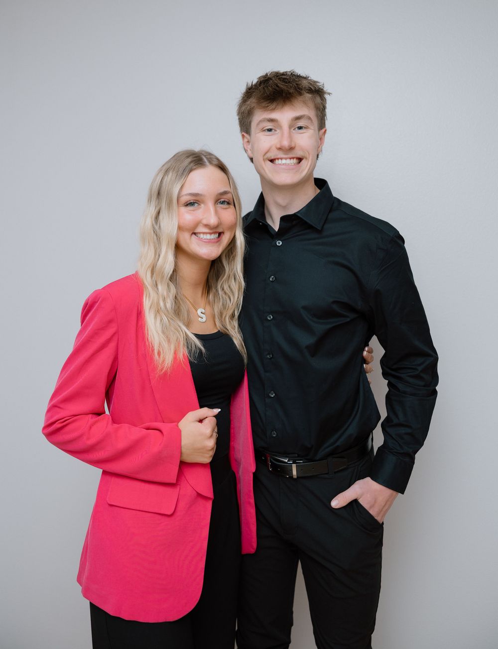 Studio portrait with bright pink blazer and black formal wear against grey background.
