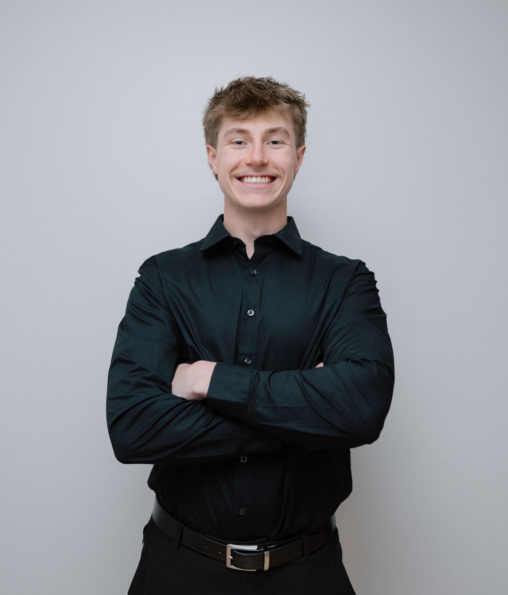 Professional headshot in black button-up shirt against neutral grey background.
