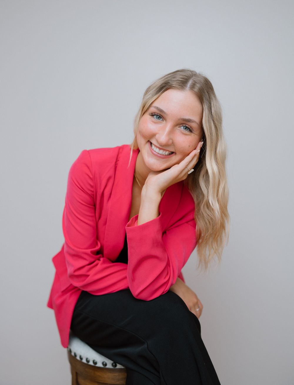 Playful studio portraits in pink blazer against grey backdrop.
