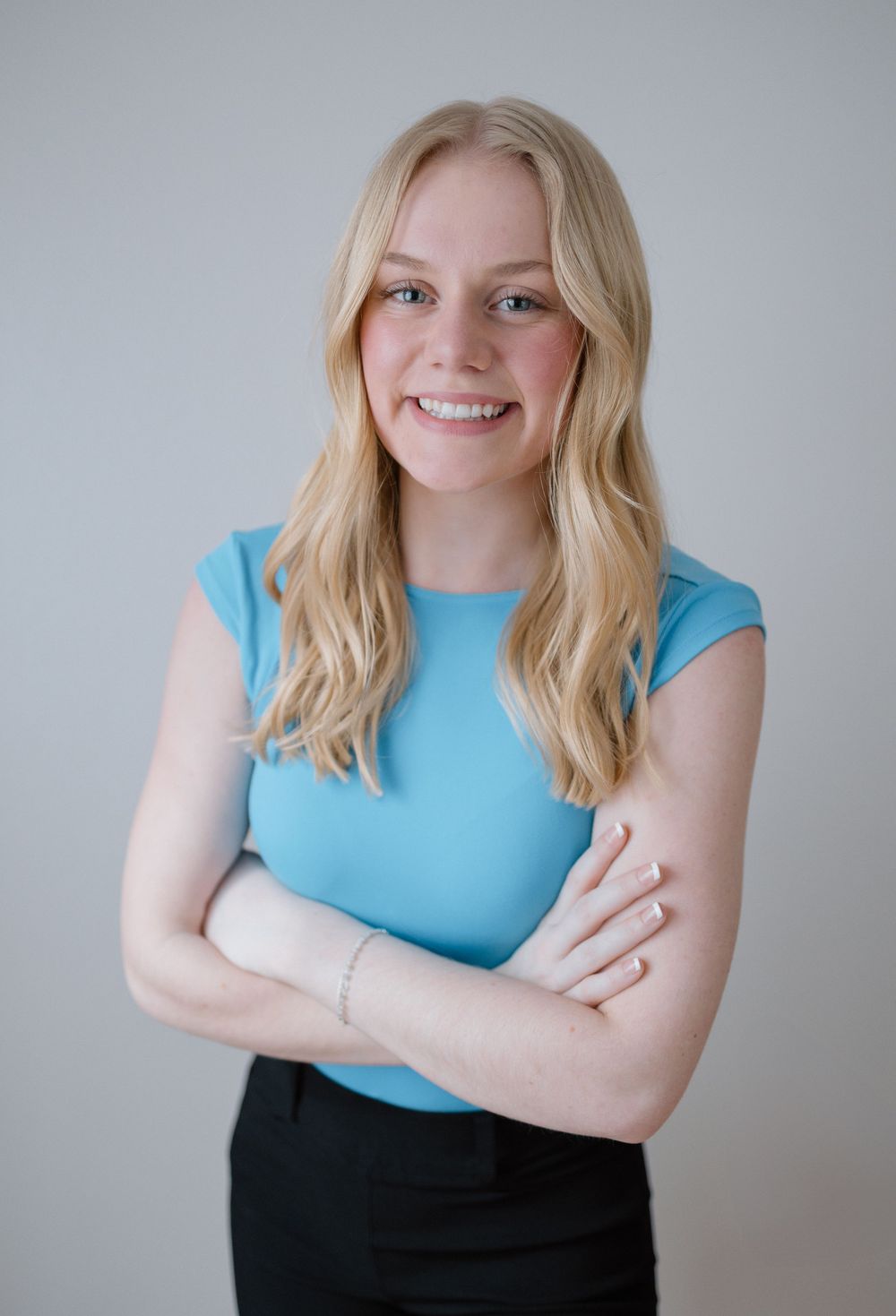 Business portraits of person wearing light blue top against neutral backdrop.