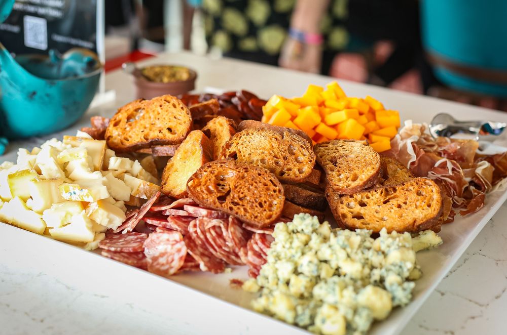 Appetizer platter with assorted cheeses, meats, crackers and dried fruit arranged on a white serving plate.