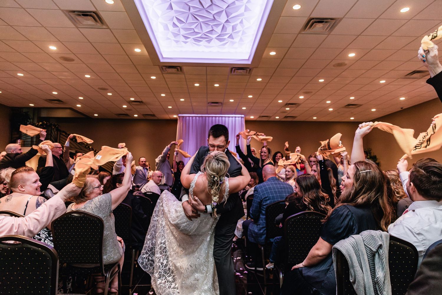 Wedding guests raise their hands and dance enthusiastically during a lively reception celebration in an elegant ballroom.