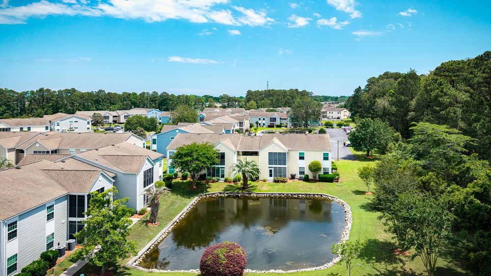 Aerial view of coastal residential community with homes surrounding a central pond.
