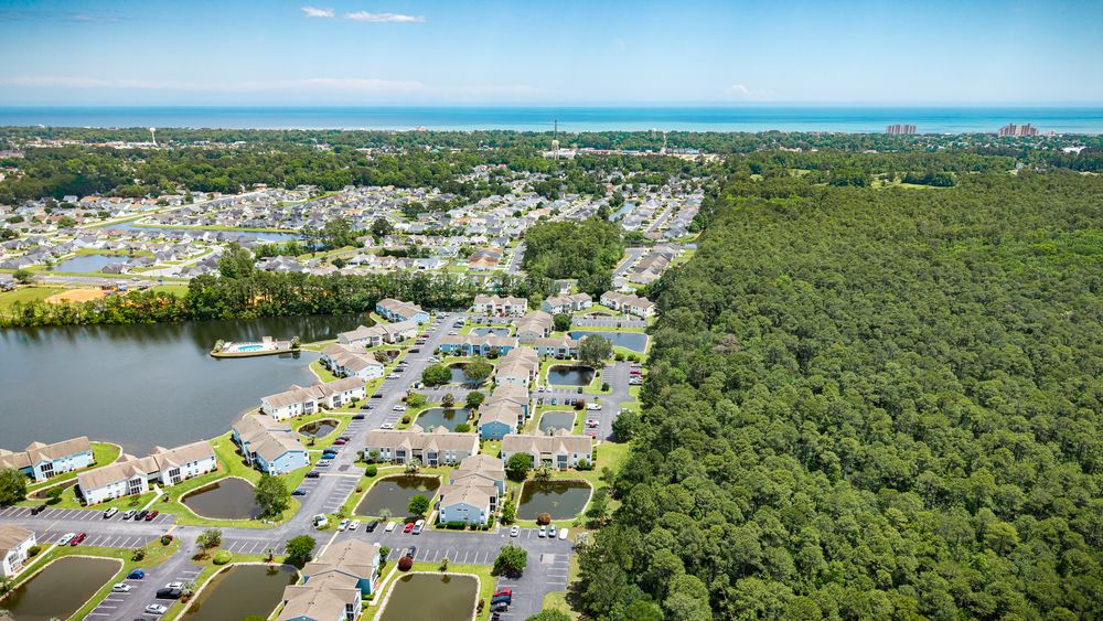 Bird's eye view of coastal neighborhood surrounded by dense forest and waterways.