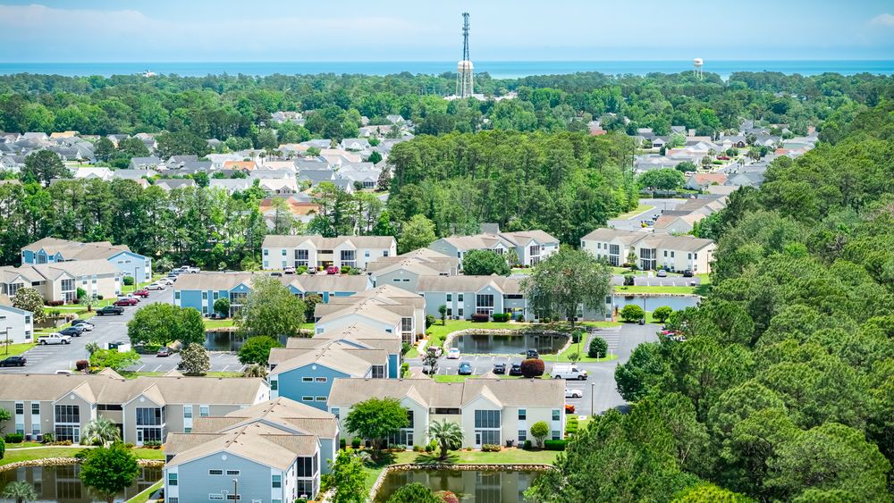 Aerial photograph of residential community nestled among pine forests with roads and buildings.