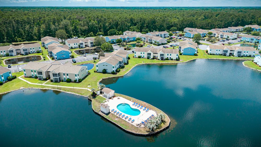 Aerial view of a waterfront residential community with a pool on a peninsula surrounded by blue water and green landscape.