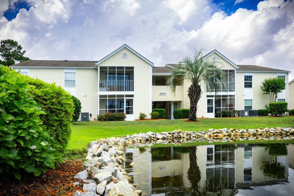 White apartment complex with palm trees and landscaped pond reflecting the building's architecture.