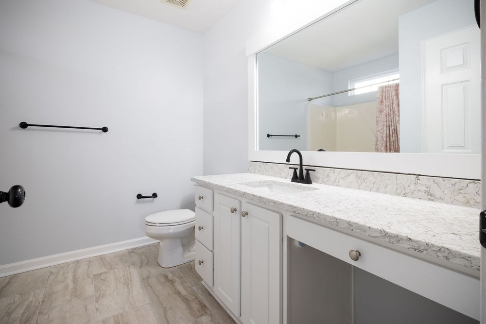 Modern white bathroom with marble countertop, toilet and simple fixtures.