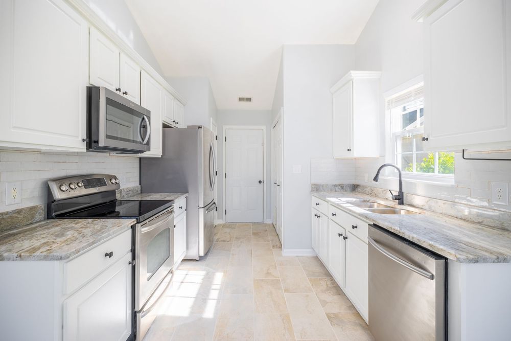 Bright white galley kitchen with stainless appliances and marble countertops.