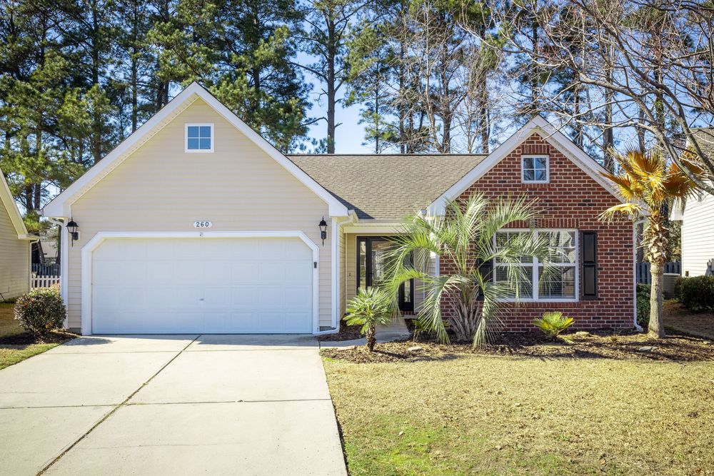 Tan and brick single story home with white garage door and palm tree landscaping.