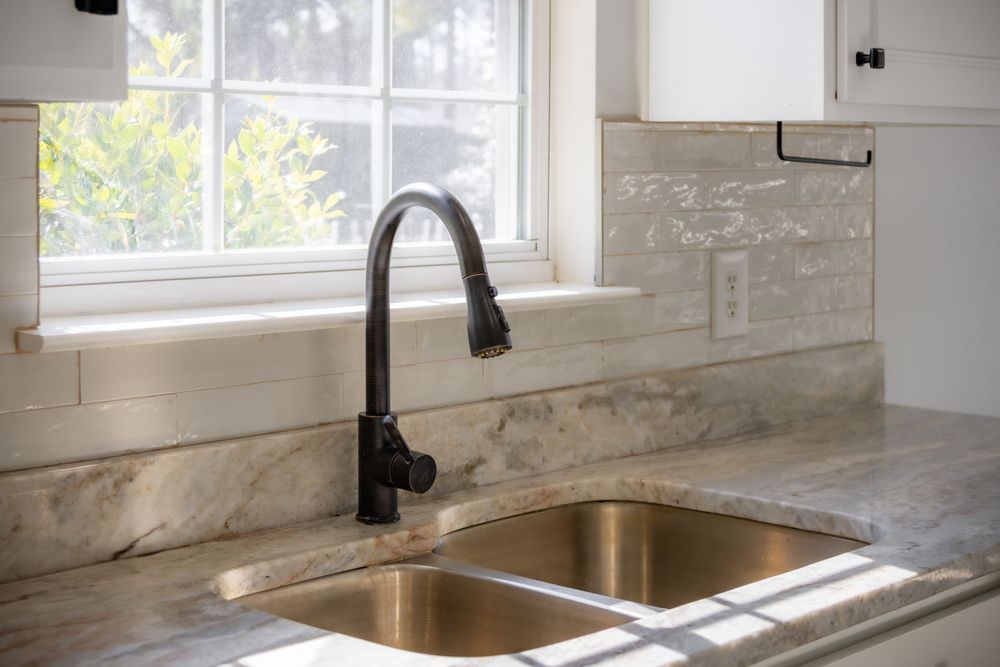 Close-up of modern black faucet and undermount sink with marble countertop.