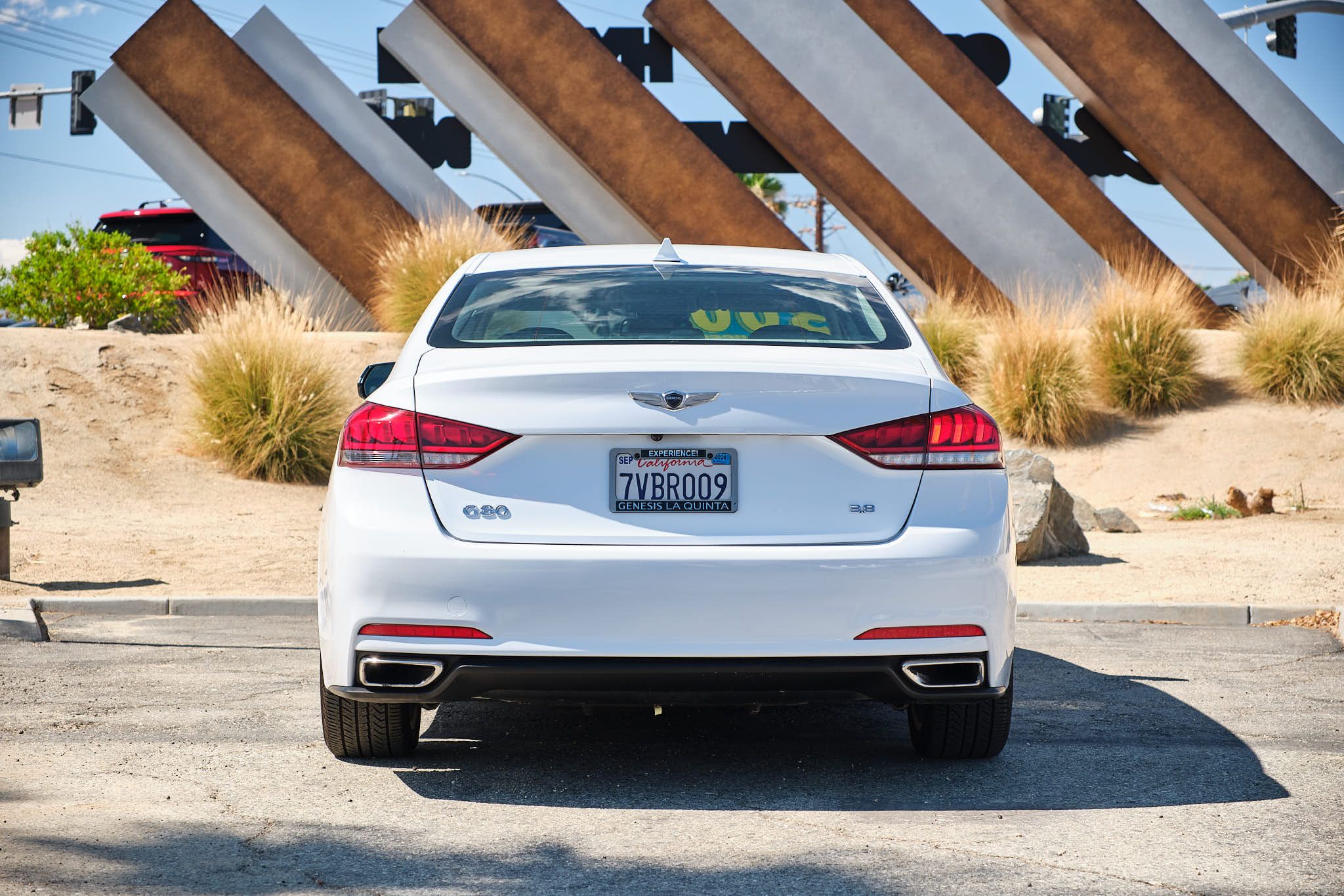 Rear view of a white Genesis G80 luxury sedan parked in front of angled architectural elements and desert landscaping.