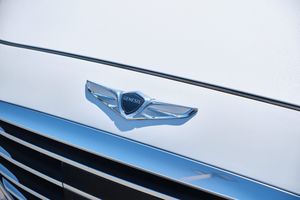 Close-up view of the Genesis Wings logo emblem mounted on a white vehicle exterior.