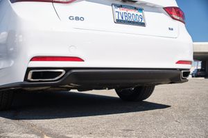 Close-up view of a white Genesis G80 luxury sedan's rear bumper showing dual exhaust tips and license plate.
