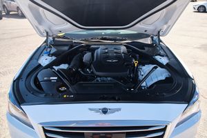 Open hood reveals powerful engine bay of a Genesis luxury vehicle with chrome trim and black components.