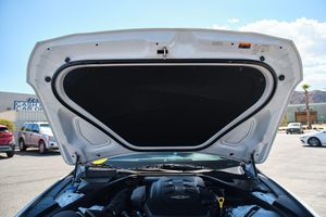 Open white car hood showing engine bay compartment against blue sky.
