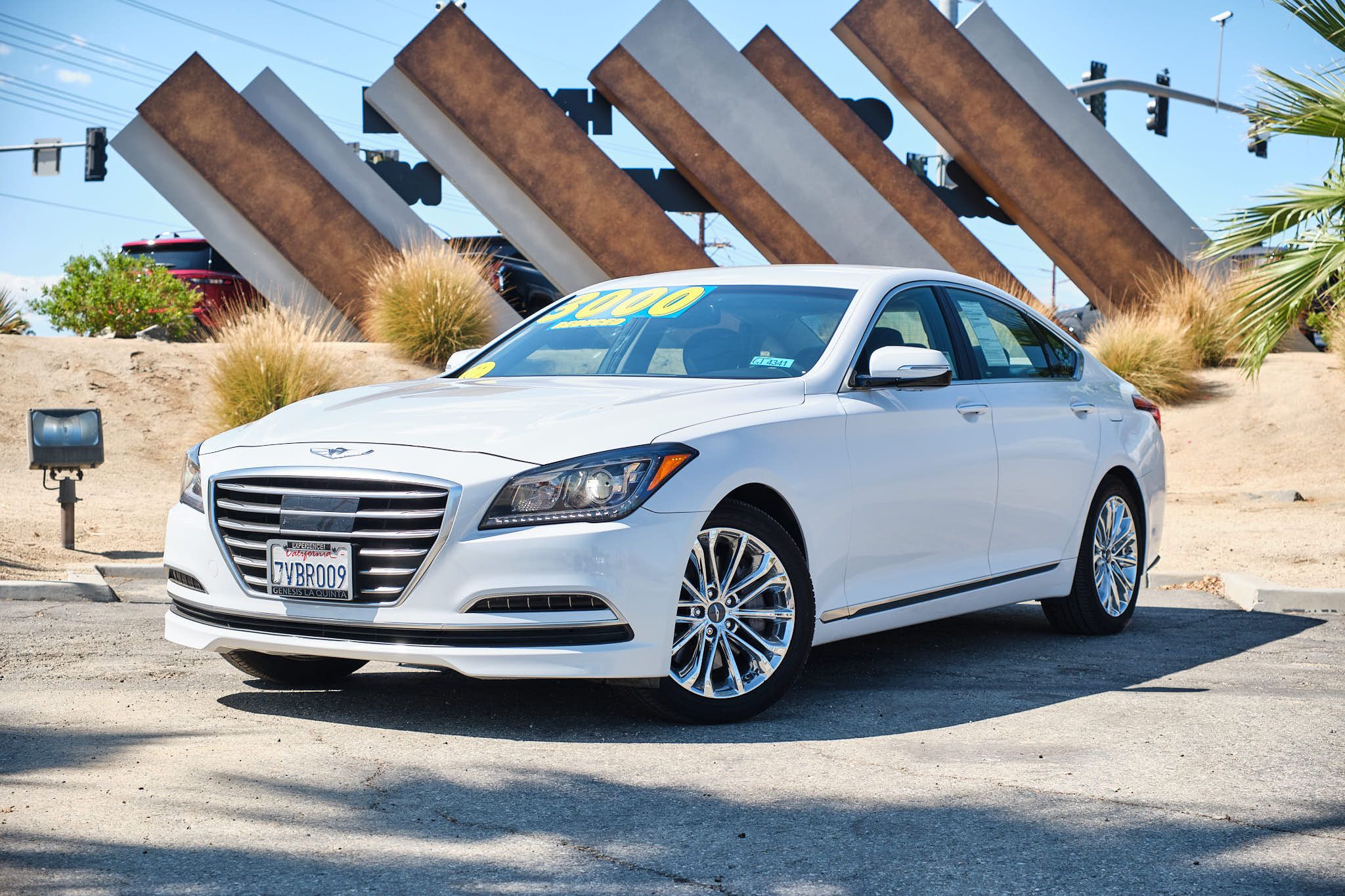 White Hyundai Genesis G80 luxury sedan parked in front of modern angular architectural feature and palm trees.