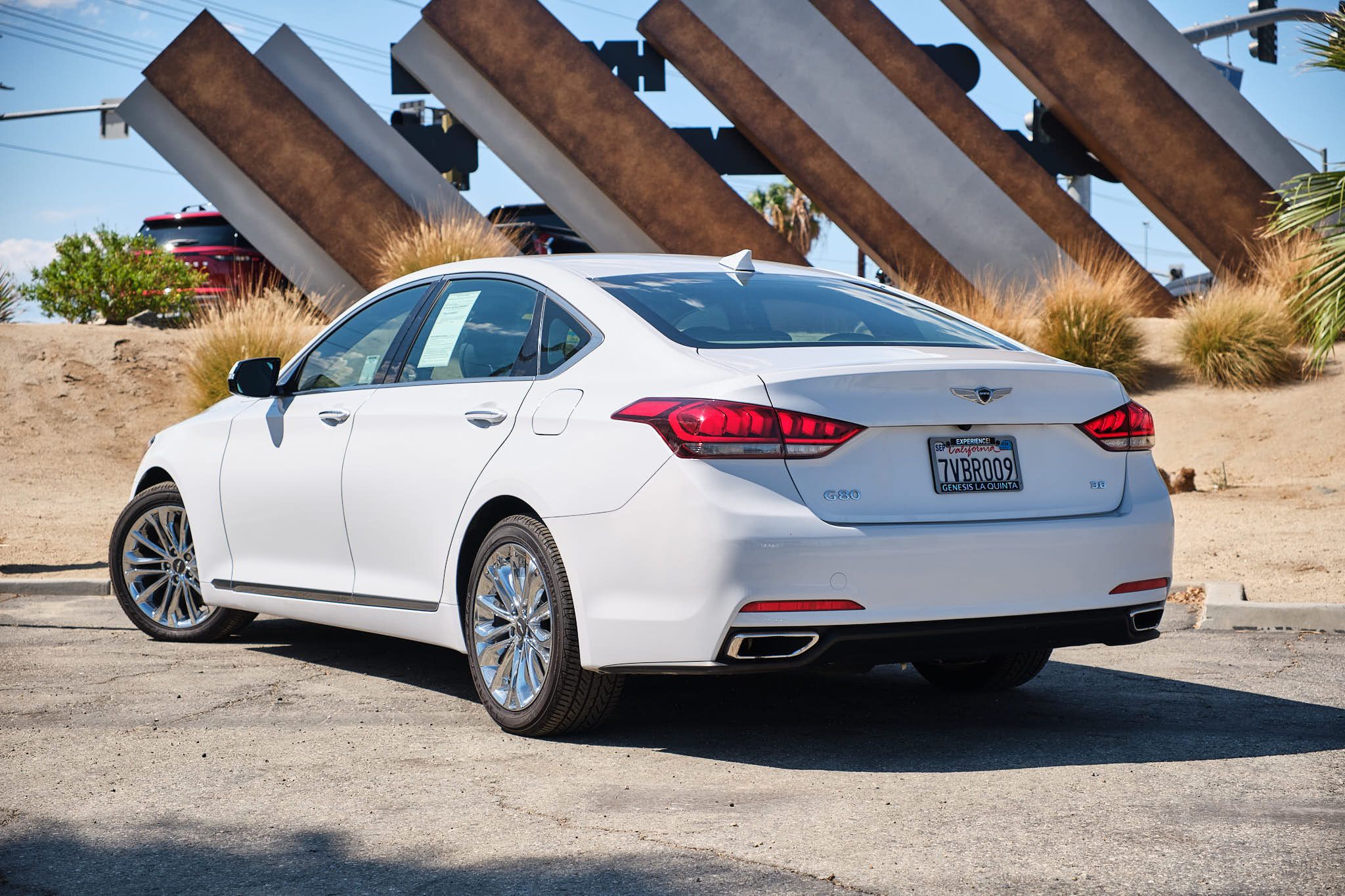 Rear three-quarter view of white Genesis G80 luxury sedan showcasing LED taillights and dual exhaust.