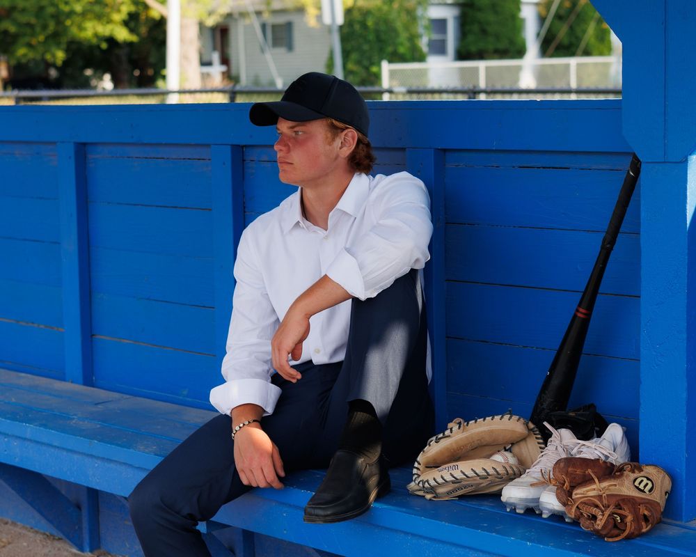 A baseball player sits on a bright blue dugout bench with baseball gloves and equipment beside them.