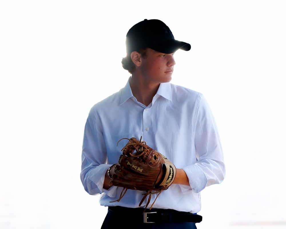 Baseball player in white uniform winds up for a pitch against bright white background.