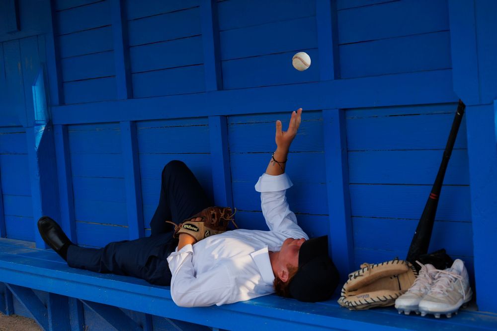 A person in a white shirt lies on a blue bench reaching up towards a bright full moon in the night sky.