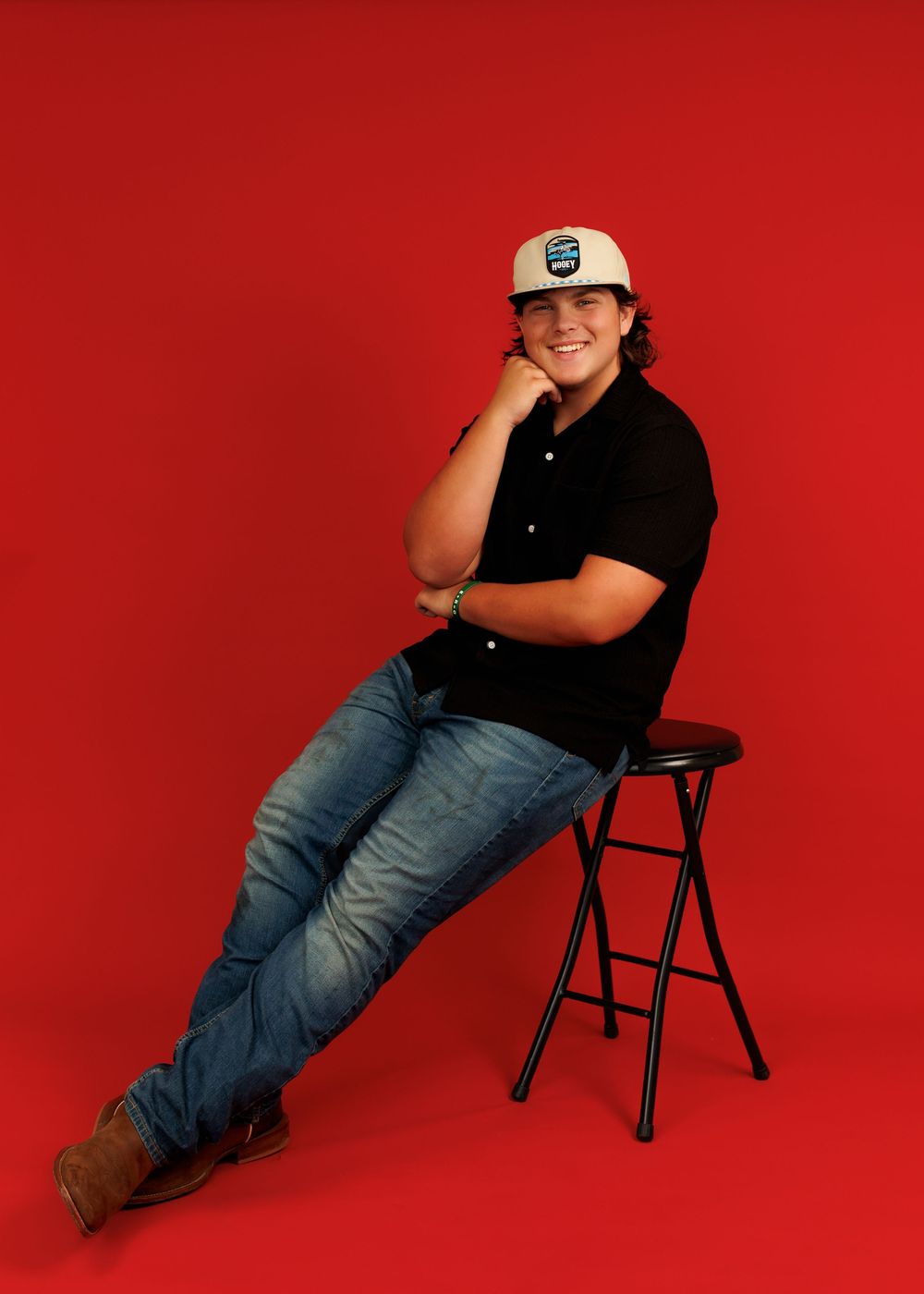 A person in black shirt and jeans poses in four different relaxed positions on a folding chair against a bright red backdrop.