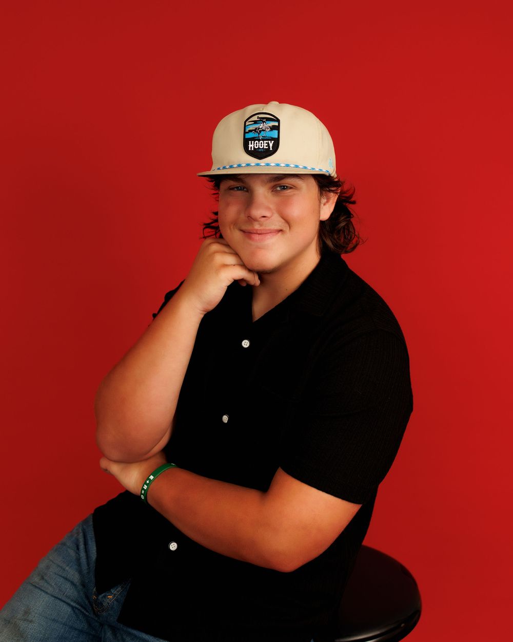 Portrait series against a red background showing casual poses in black shirt and baseball cap.