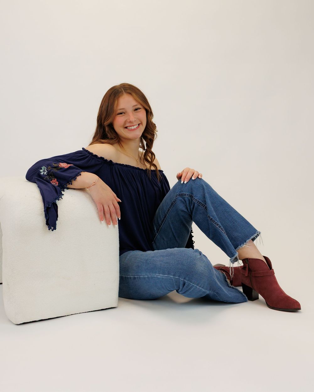 A relaxed casual portrait against a white background showing off a navy top, jeans and burgundy ankle boots.