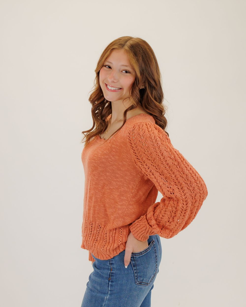 Someone wearing a cozy orange knit sweater with puff sleeves and blue jeans poses against a white backdrop.