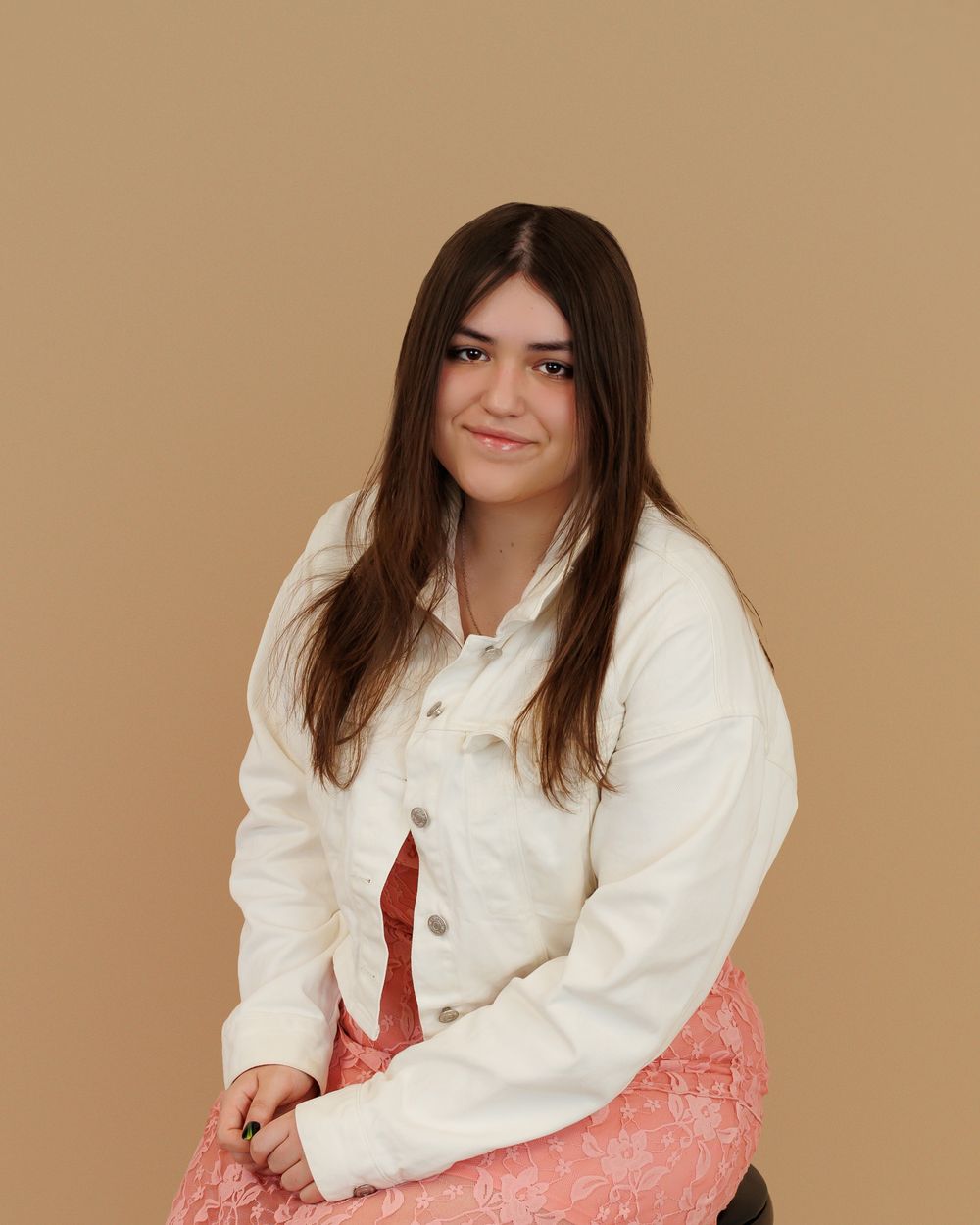 Subject wearing a white button-up jacket poses against beige backdrop with long brown hair and pink bottoms.