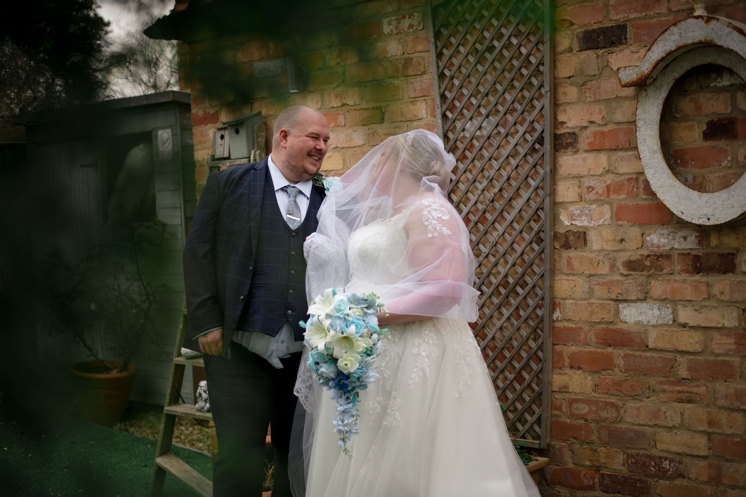Couple shares tender moment together at their outdoor wedding ceremony near rustic brick wall with hanging flowers.