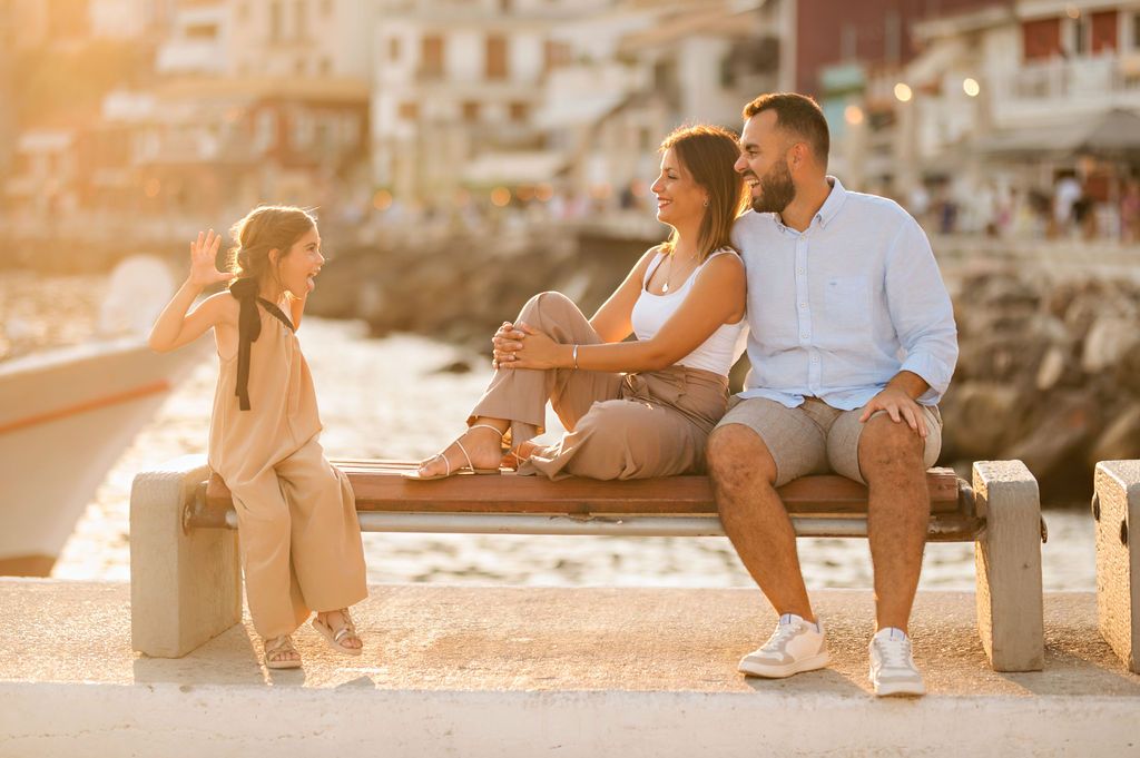 Family enjoying sunset together on a harbor bench in a Mediterranean coastal town.