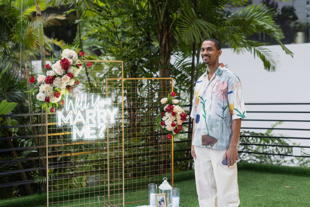 Outdoor proposal setup featuring neon sign and white mesh backdrop decorated with red roses.