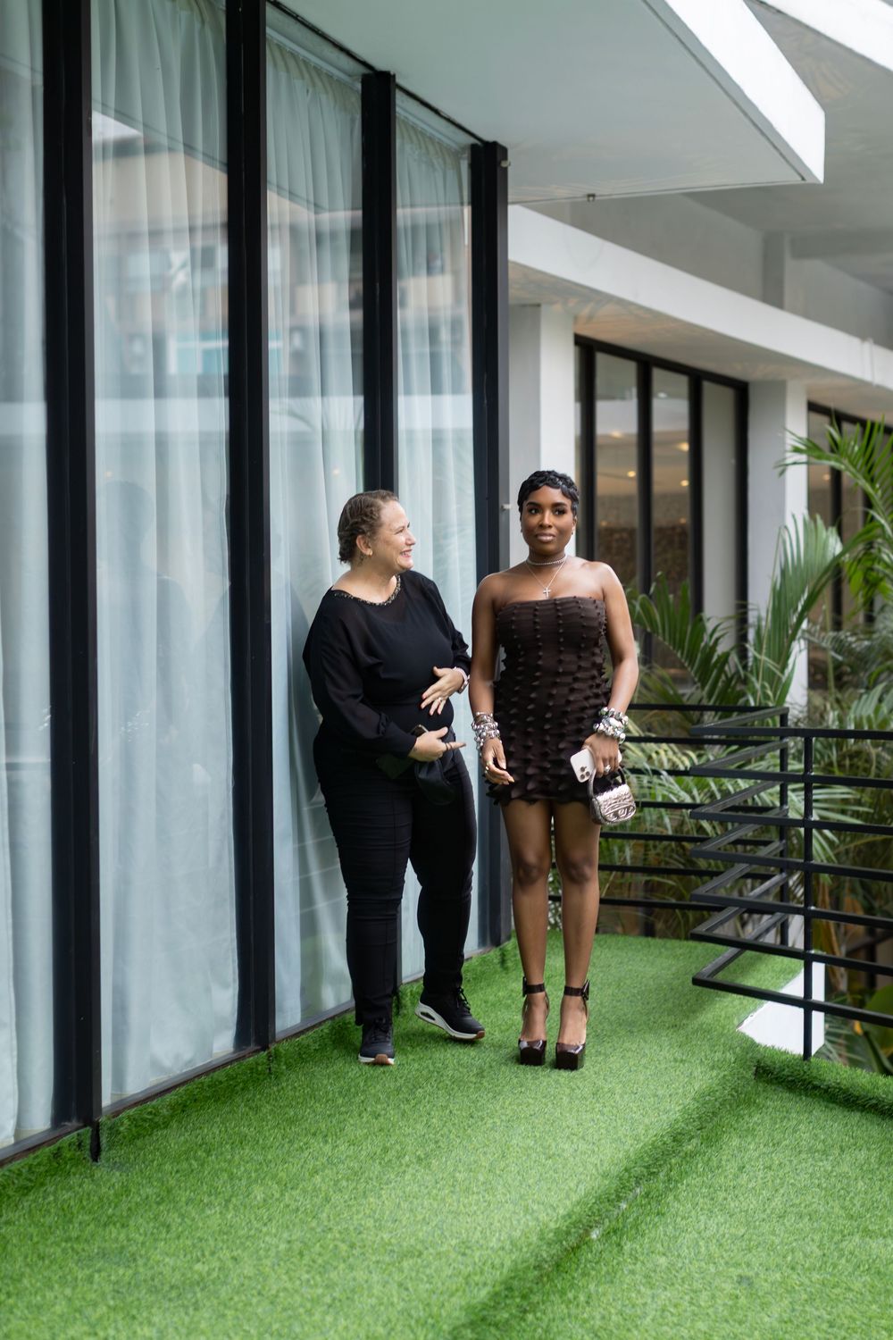 Two friends walking together on a green carpeted balcony area next to floor-to-ceiling windows.