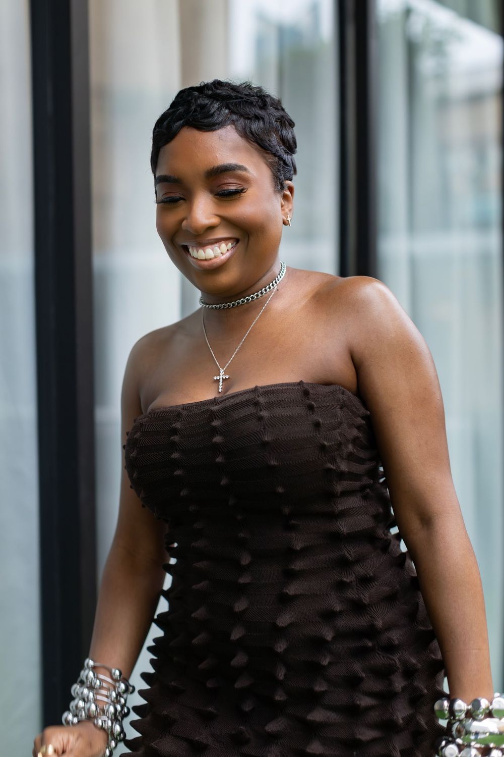 Woman in a black strapless dress smiling while wearing layered necklaces and jewelry.