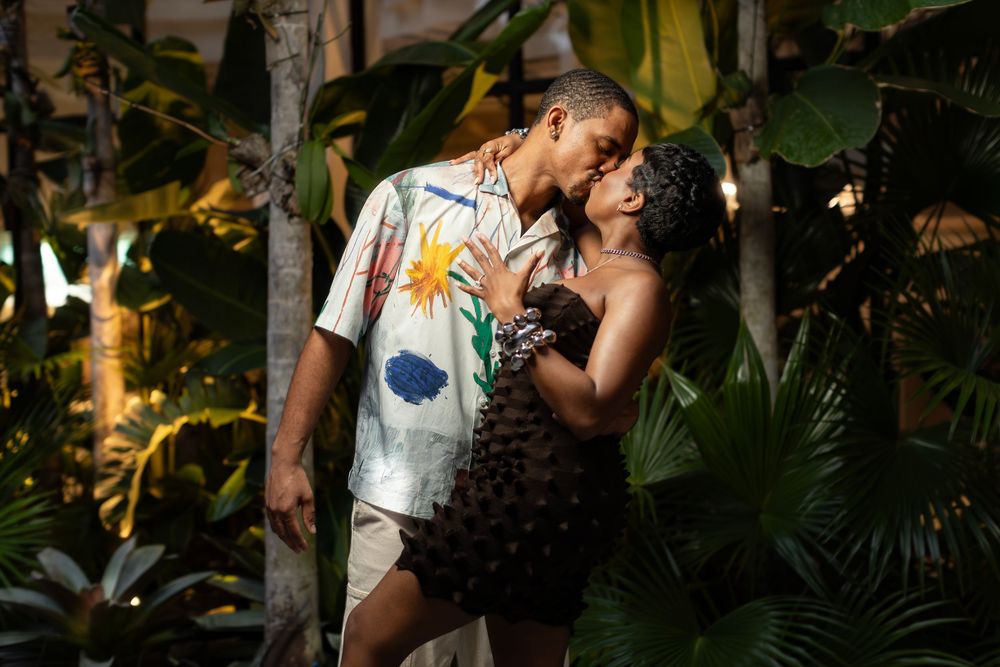 Romantic couple sharing intimate moment among tropical plants and natural setting.