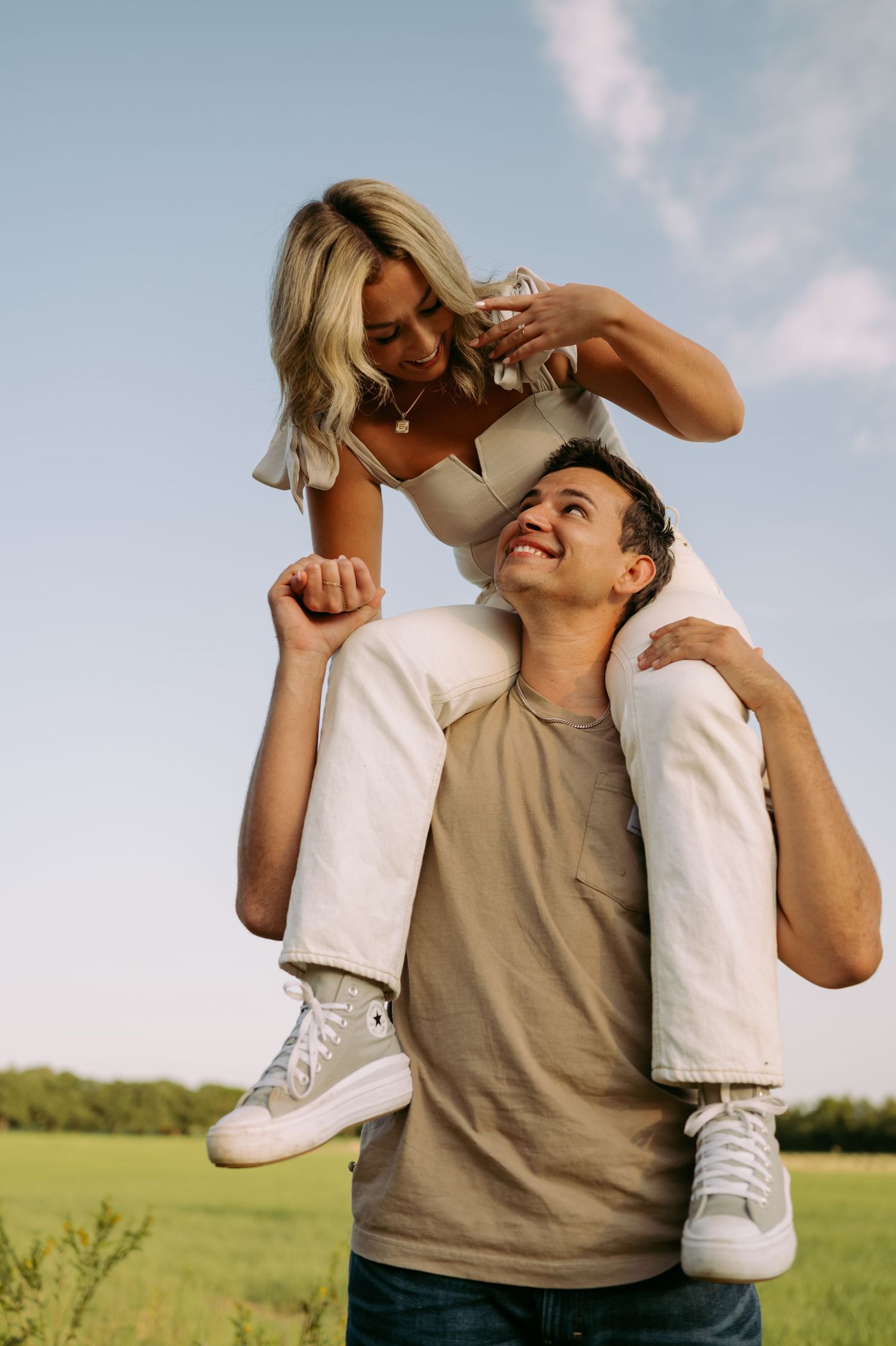 A playful couple enjoying a sunny day in an open field, with one person carrying the other on their shoulders.