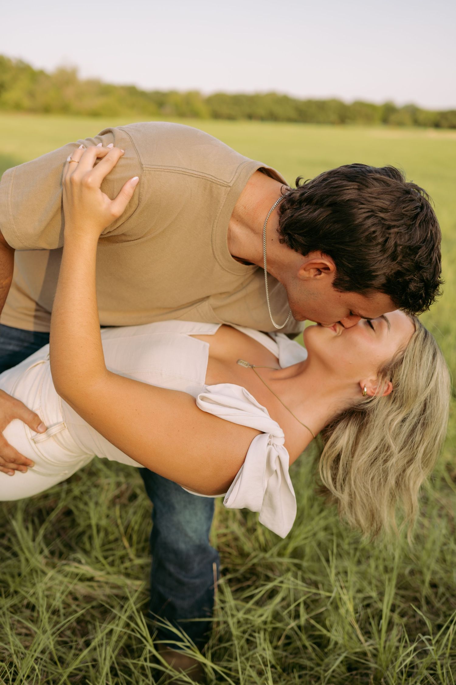 Romantic couple sharing an intimate embrace in a sunlit grassy field during golden hour.