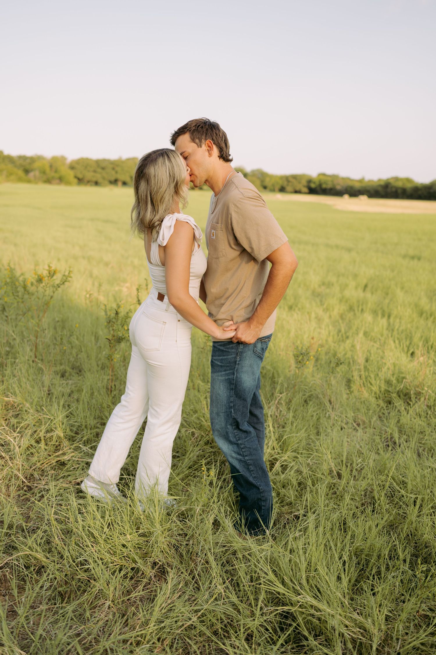 Couple in casual attire sharing a tender moment while standing in a meadow during sunset.