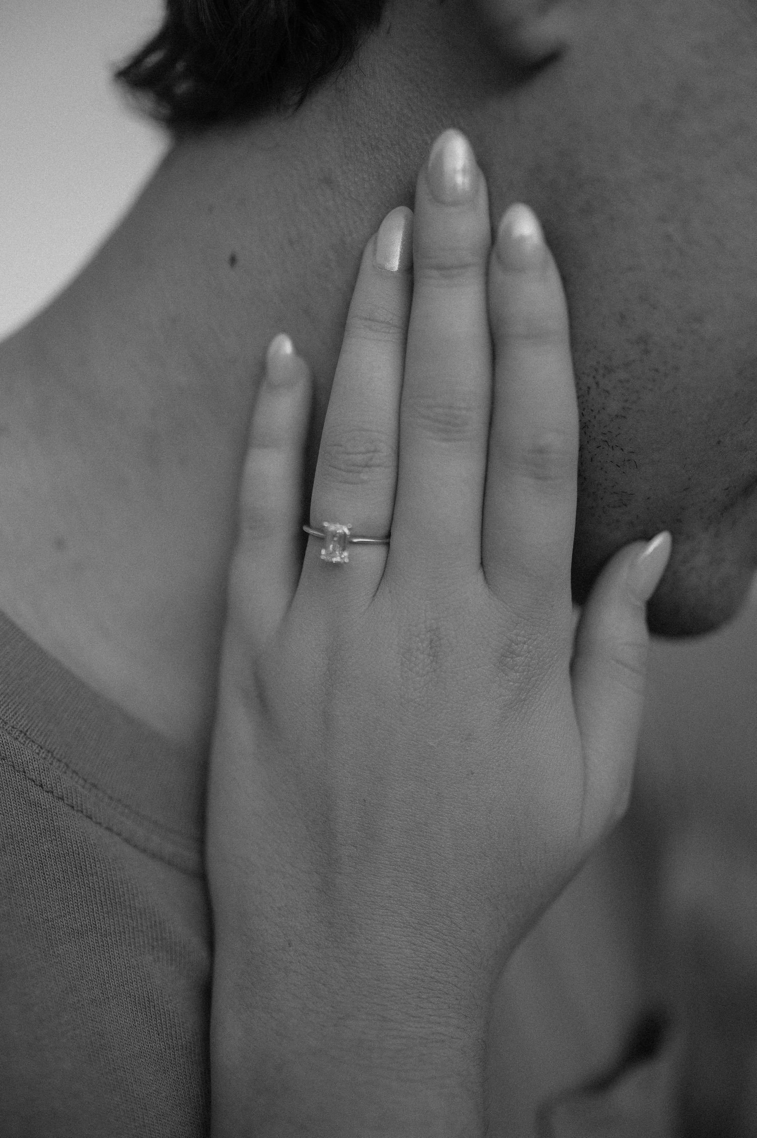 A close-up black and white photo of a hand wearing an engagement ring with perfectly manicured nails.