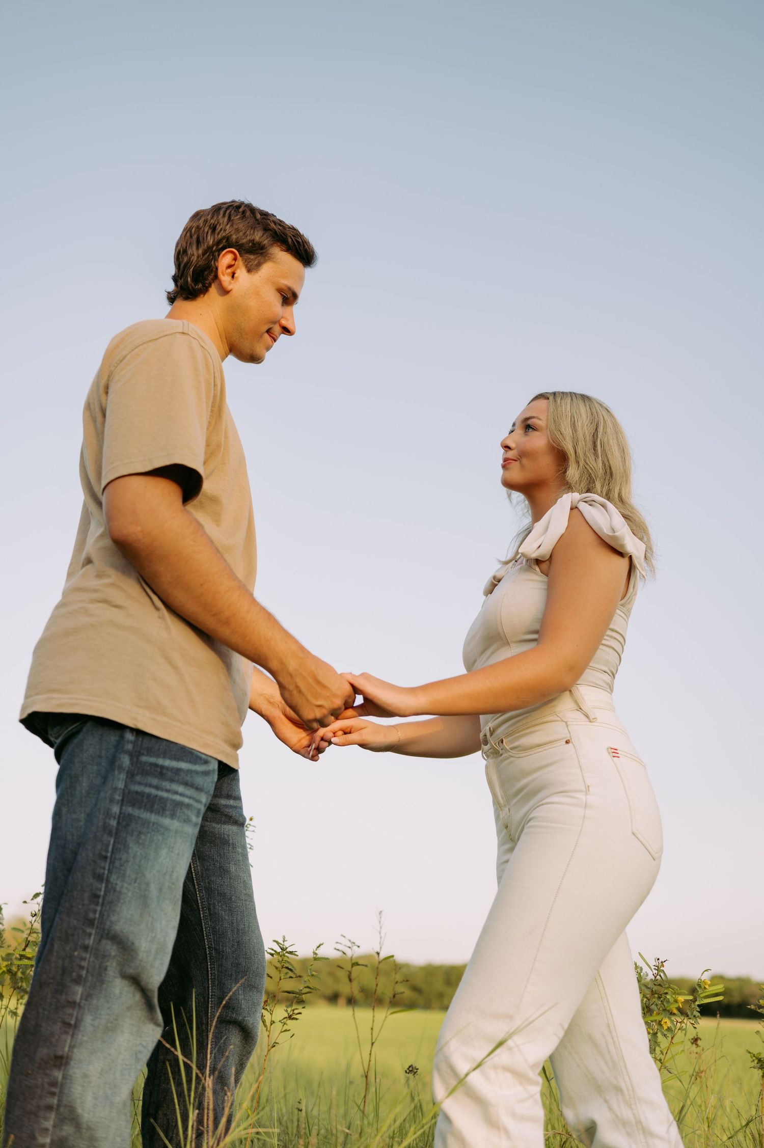 Young couple holding hands and sharing a romantic moment while standing in a lush green field on a sunny day.