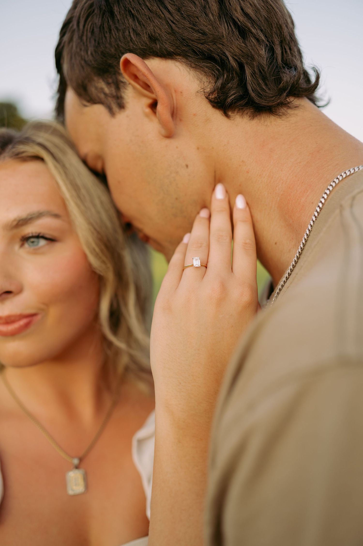 A romantic moment captured showing a couple embracing with an engagement ring visible on the woman's hand.