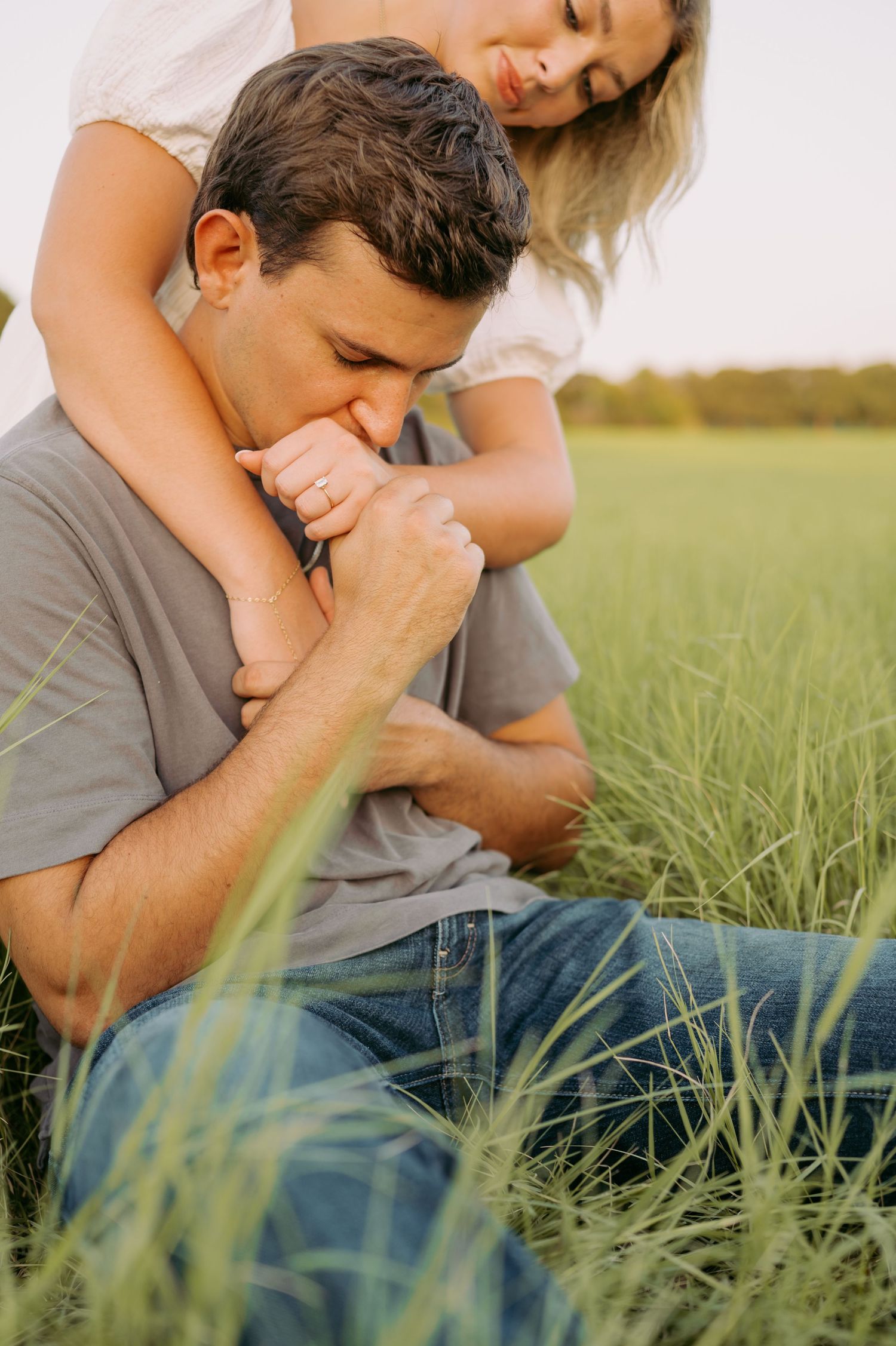 Intimate couple embraces in tall grass field during golden hour as sunlight illuminates their tender moment.