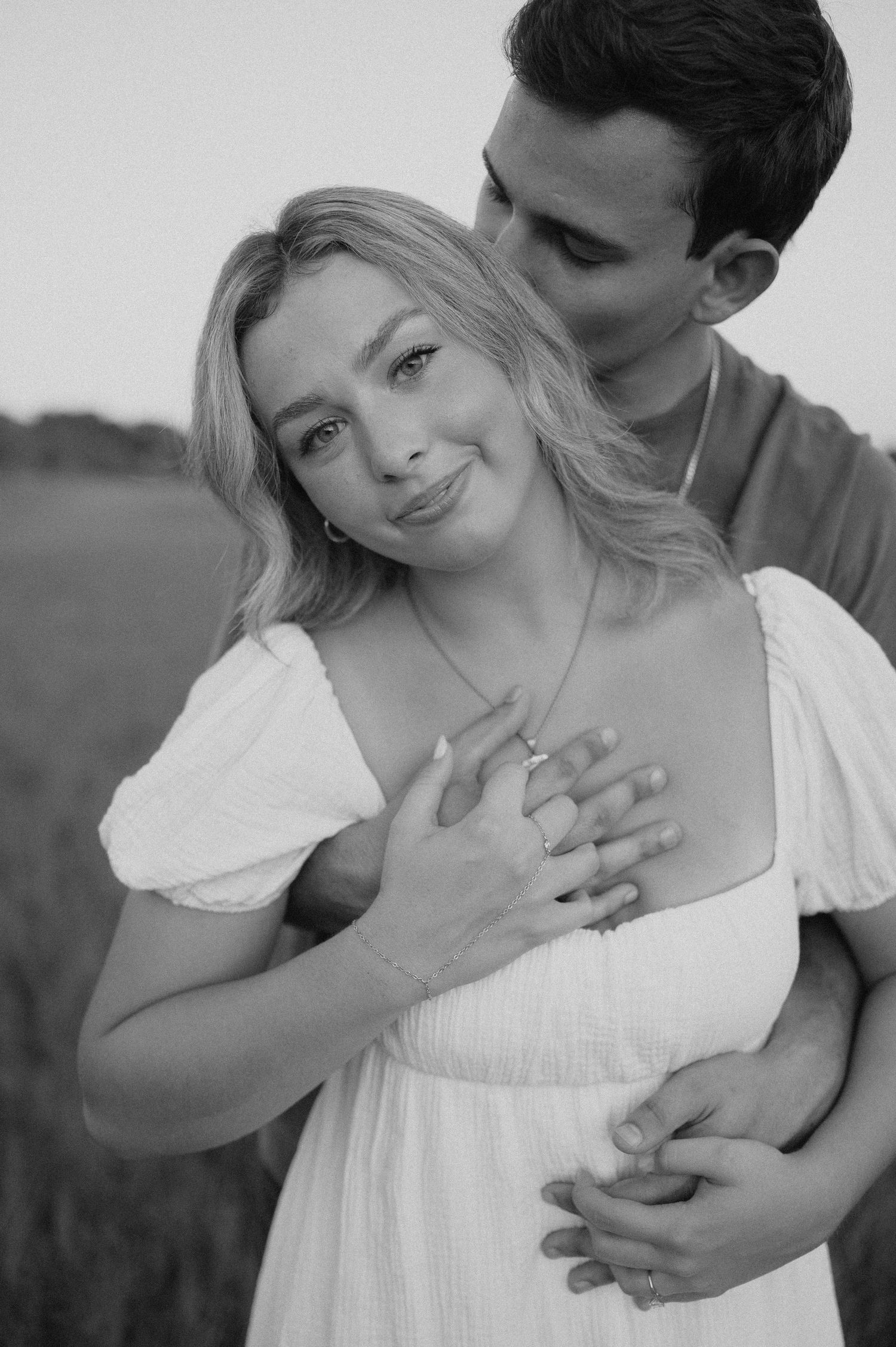 Couple shares romantic black and white portrait in field as they embrace and smile together.