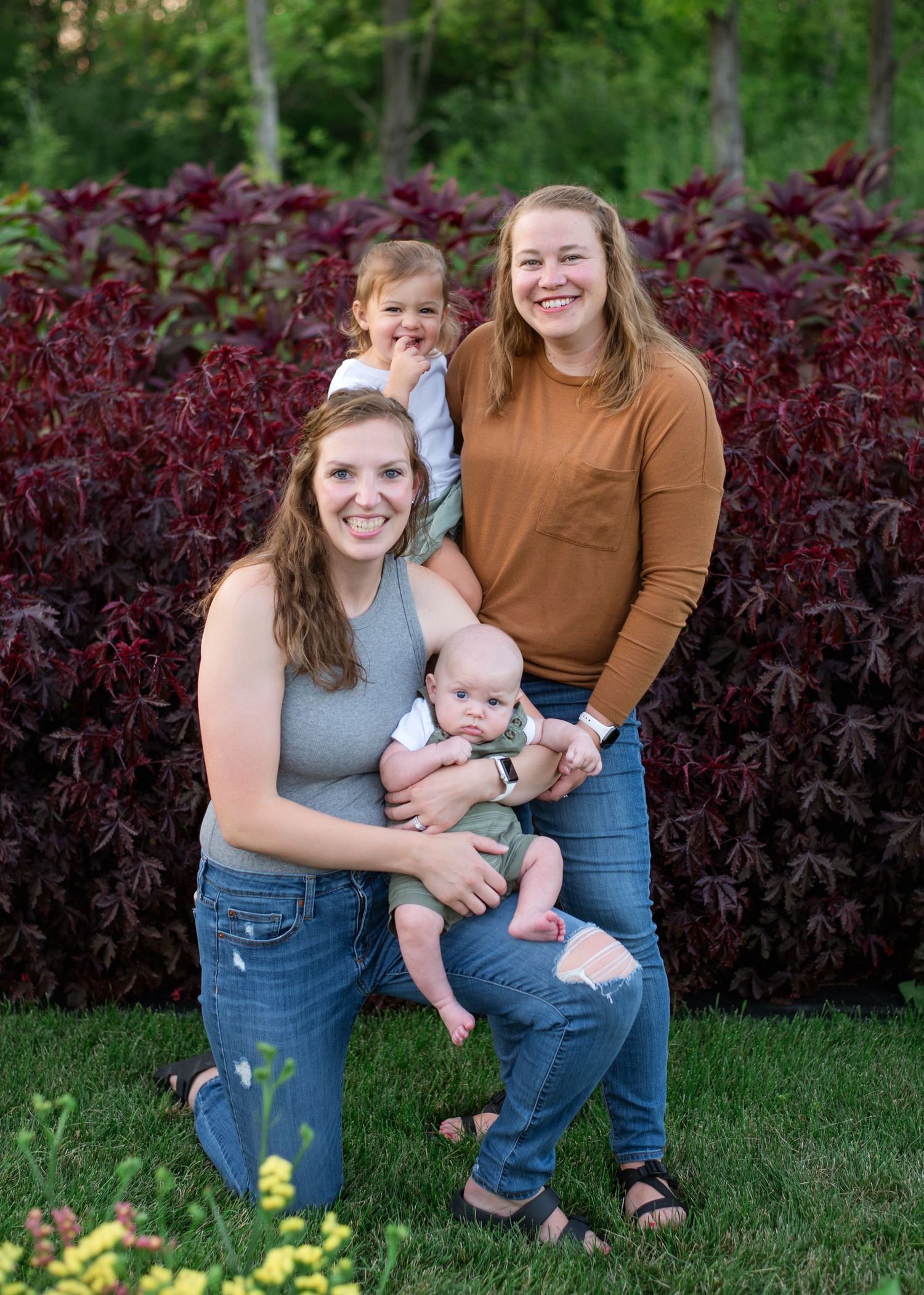 Group poses outdoors against vibrant burgundy foliage background on a sunny day in casual attire.