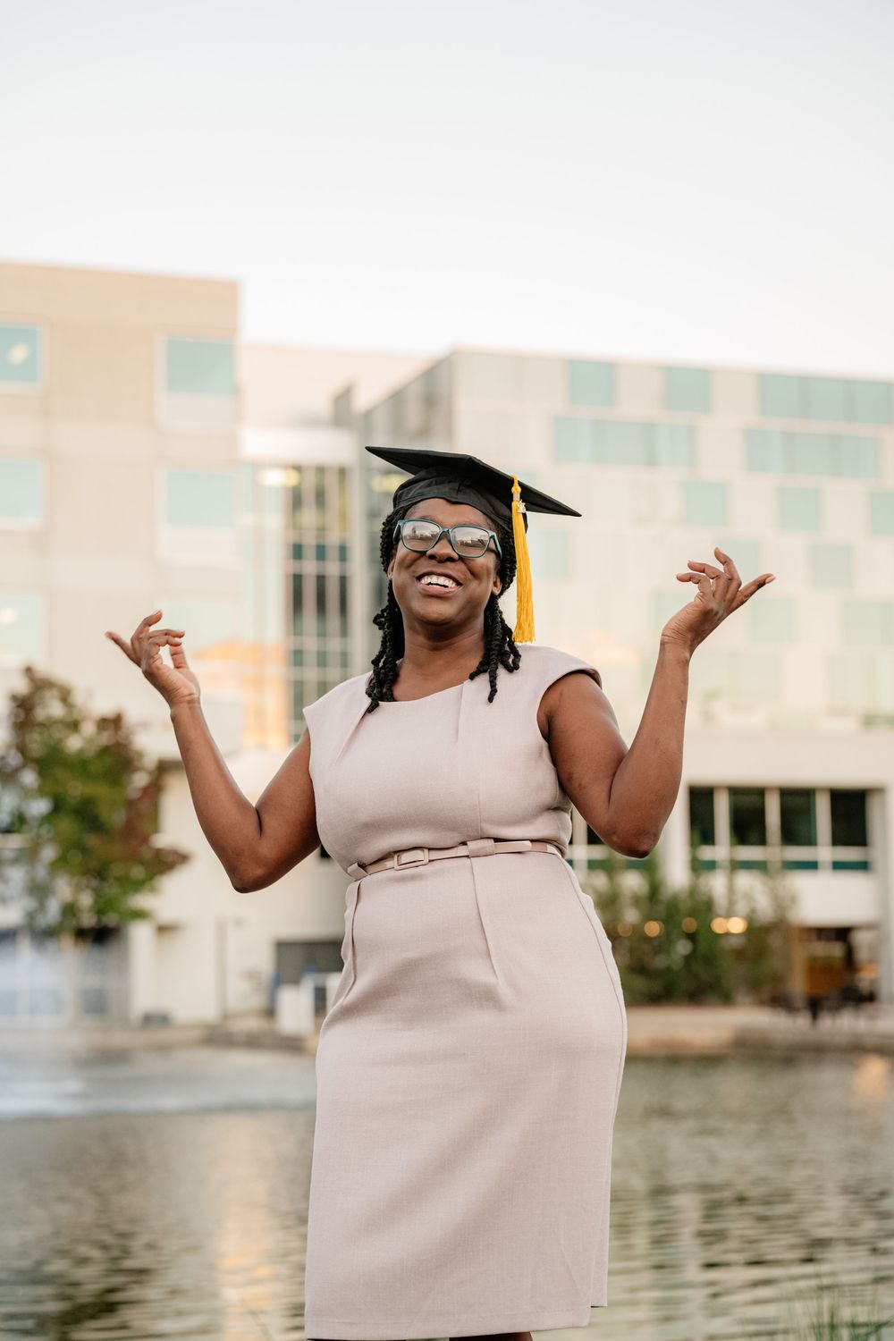 senior posing with hands up in front of water and buildings