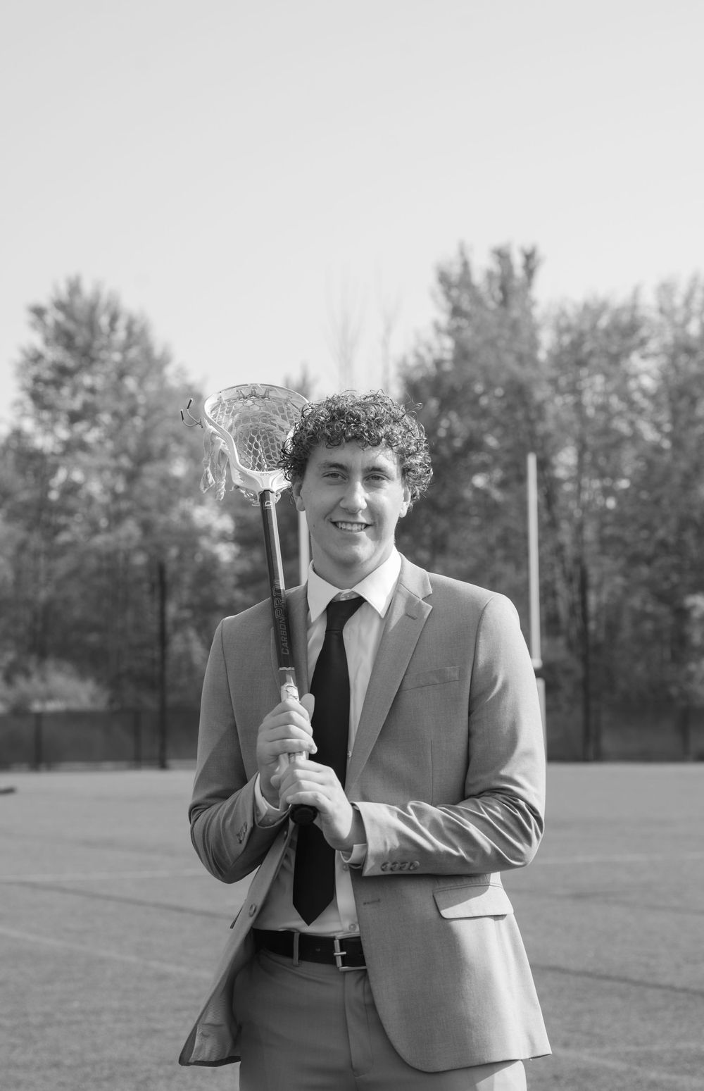 senior in a suit with his lacrosse stick